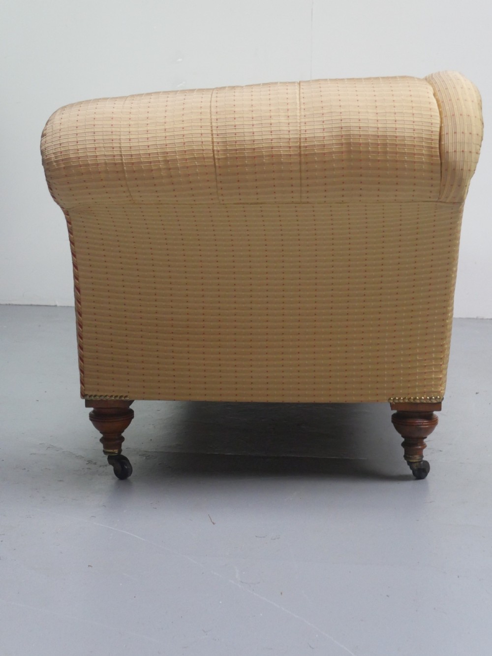 A 19th-century Victorian chaise longue upholstered in a yellow patterned fabric with deep buttoning on the curved backrest and turned mahogany legs on brass castors. View XI
