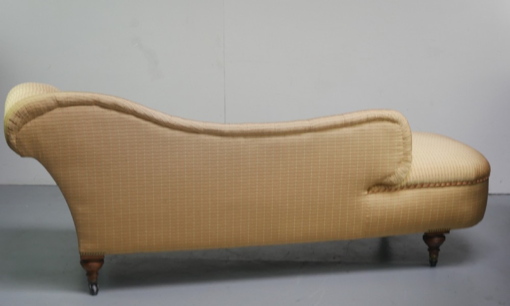 A 19th-century Victorian chaise longue upholstered in a yellow patterned fabric with deep buttoning on the curved backrest and turned mahogany legs on brass castors. View XII