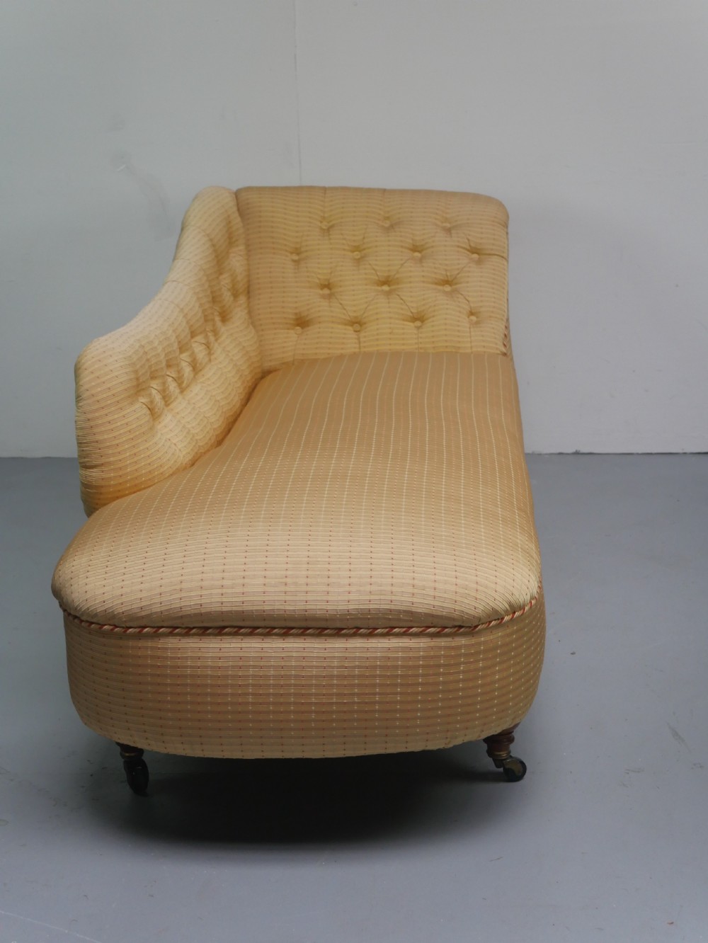 A 19th-century Victorian chaise longue upholstered in a yellow patterned fabric with deep buttoning on the curved backrest and turned mahogany legs on brass castors. View XIII