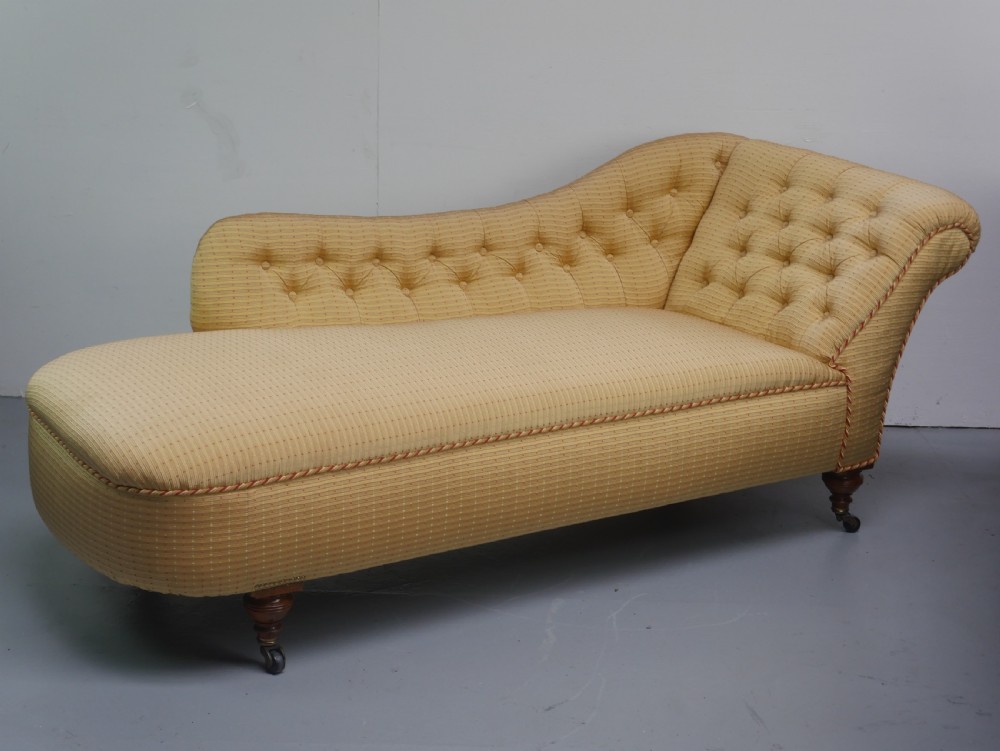A 19th-century Victorian chaise longue upholstered in a yellow patterned fabric with deep buttoning on the curved backrest and turned mahogany legs on brass castors. View XIV