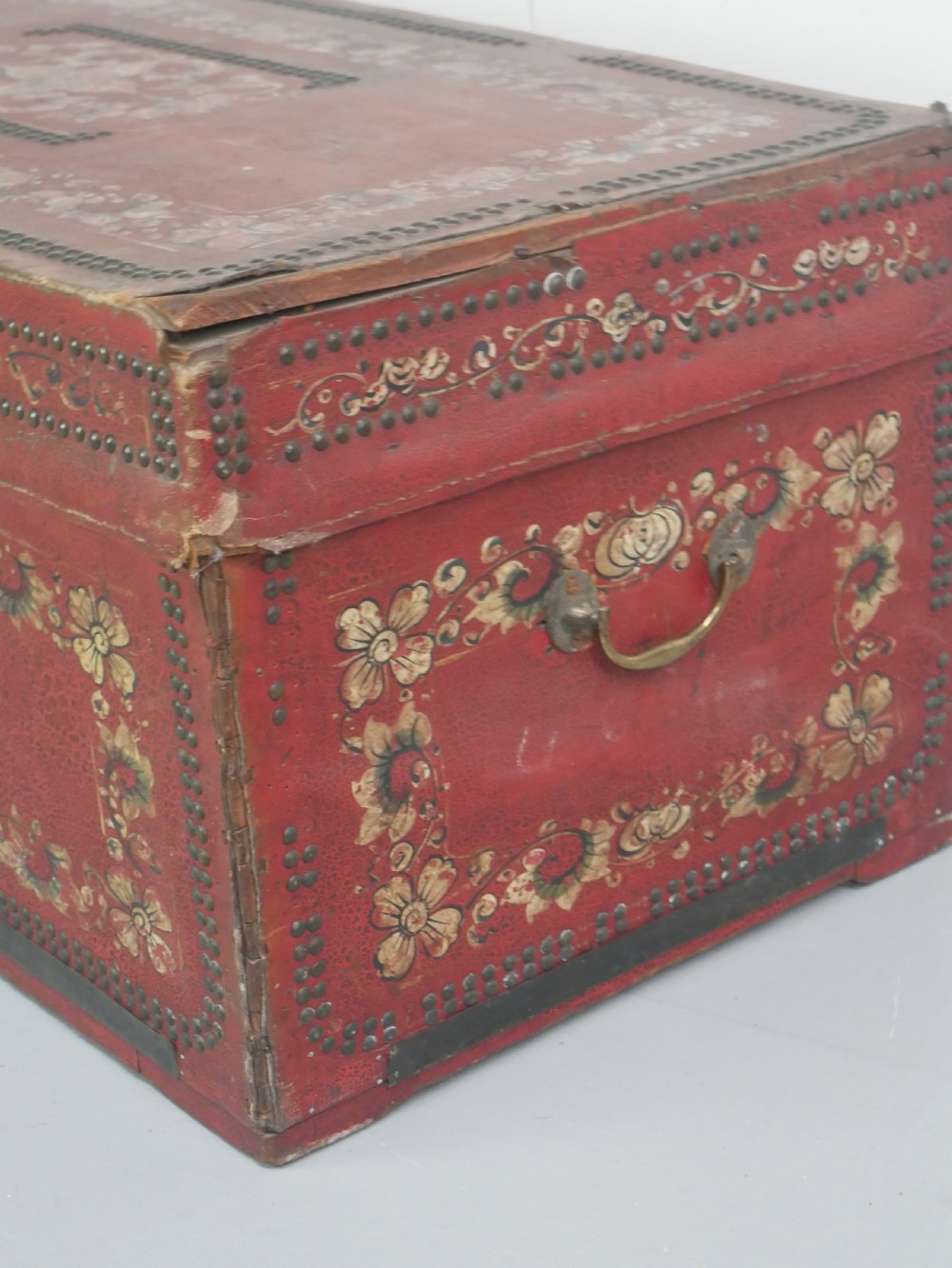 A rectangular red leather China trade trunk decorated with brass studs, brass side handles, and hand-painted gold floral motifs. View VII