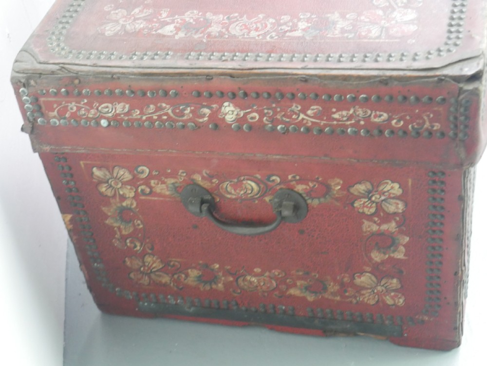 A rectangular red leather China trade trunk decorated with brass studs, brass side handles, and hand-painted gold floral motifs. View X