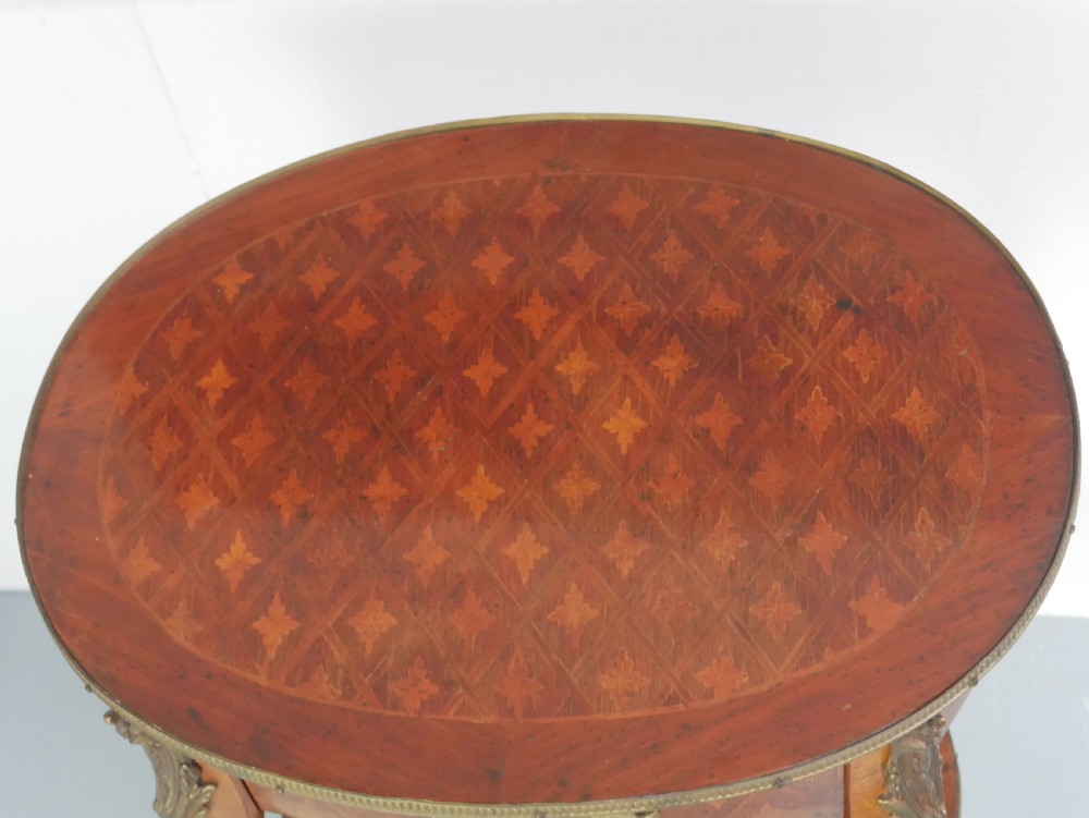 An oval Louis XV style wooden centre table featuring geometric parquetry inlay, a single drawer, a lower tier, cabriole legs, and ornate gilt metal mounts. View II