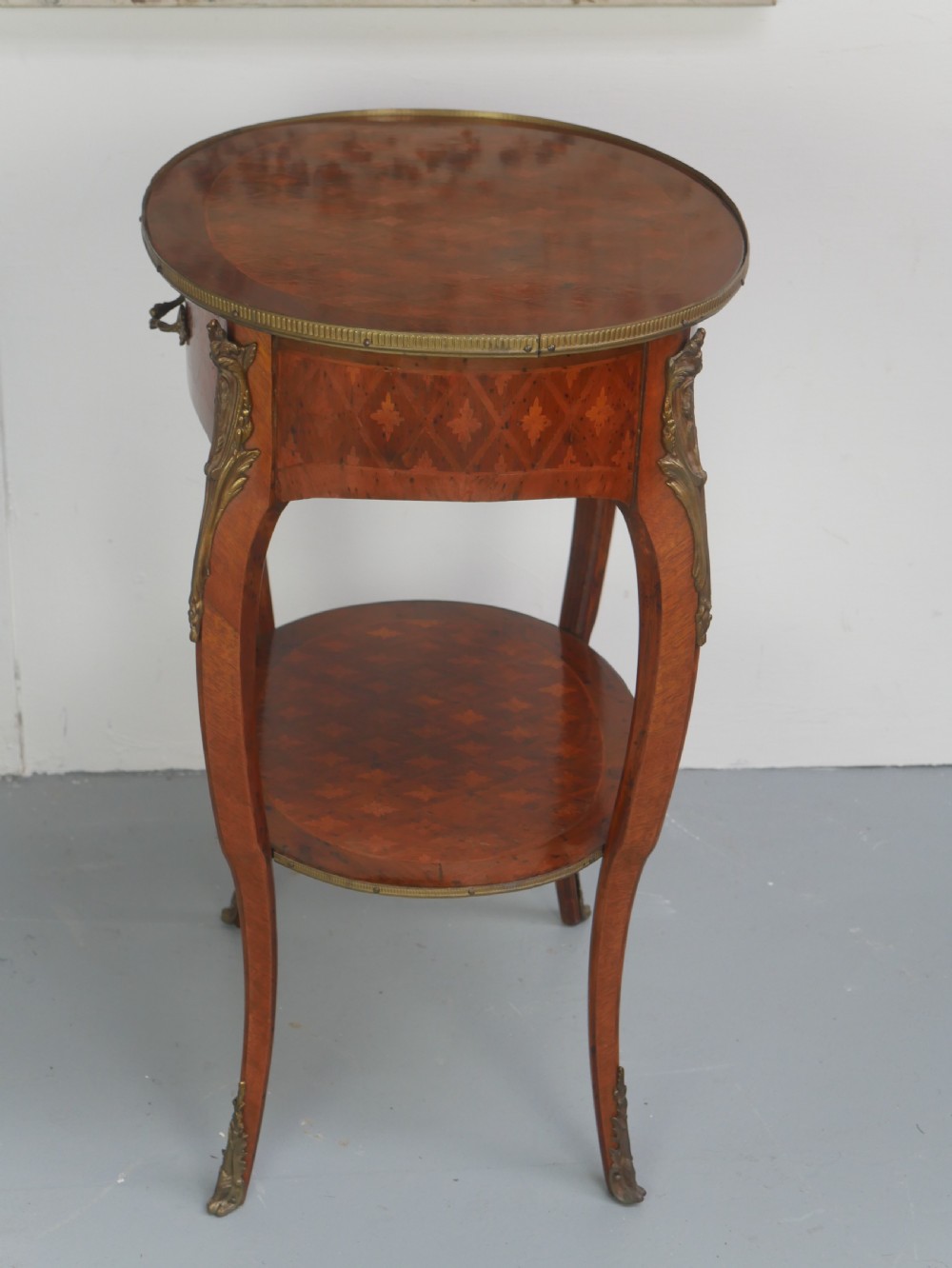 An oval Louis XV style wooden centre table featuring geometric parquetry inlay, a single drawer, a lower tier, cabriole legs, and ornate gilt metal mounts. View X