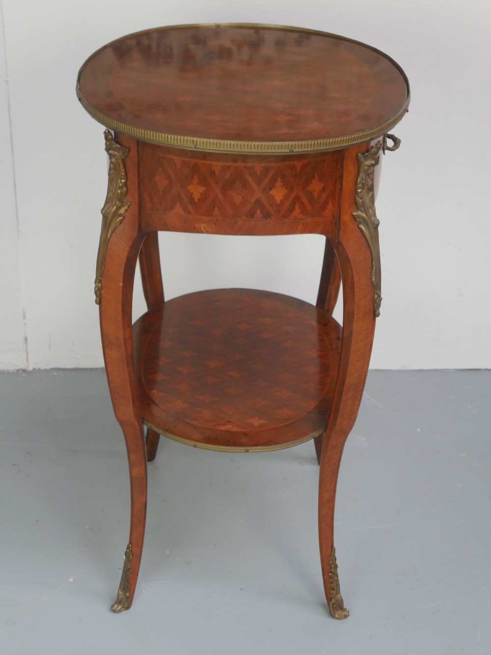 An oval Louis XV style wooden centre table featuring geometric parquetry inlay, a single drawer, a lower tier, cabriole legs, and ornate gilt metal mounts. View XII