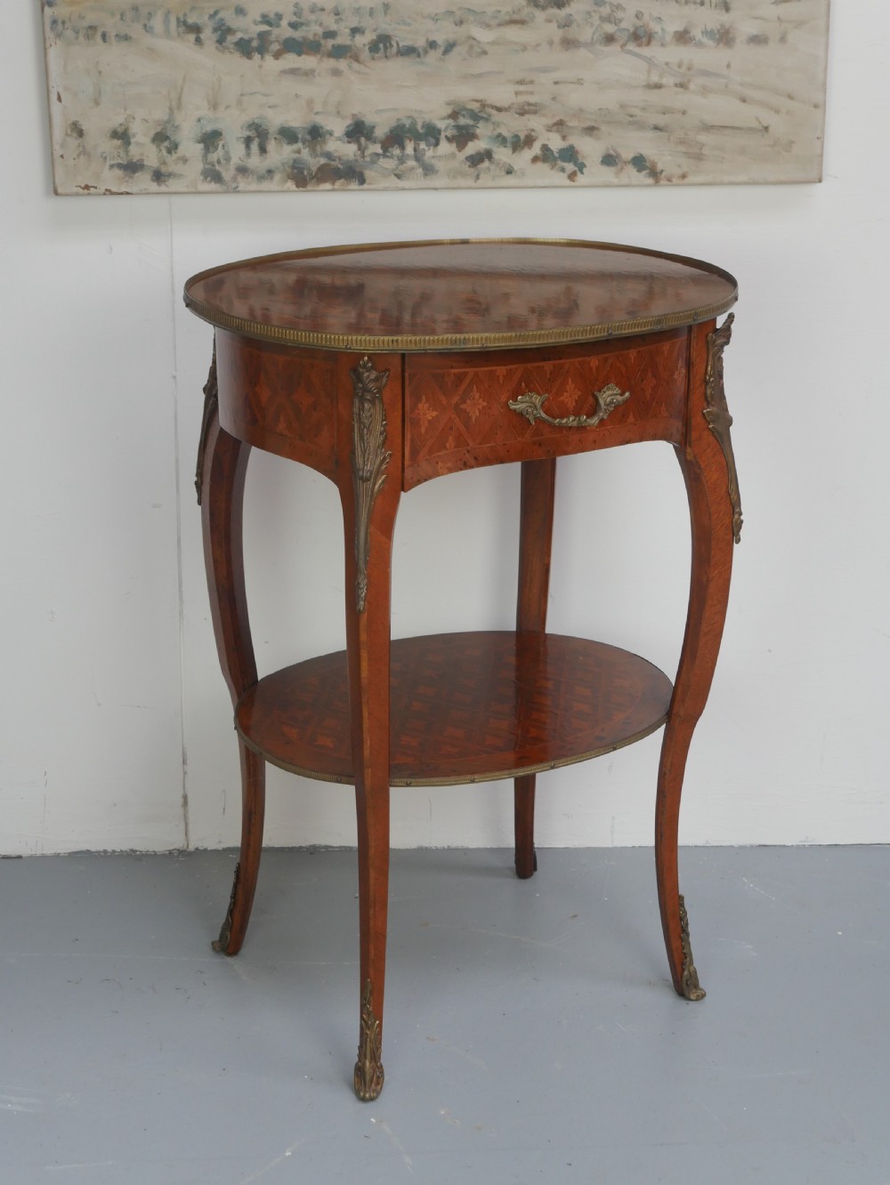 An oval Louis XV style wooden centre table featuring geometric parquetry inlay, a single drawer, a lower tier, cabriole legs, and ornate gilt metal mounts. View XIII
