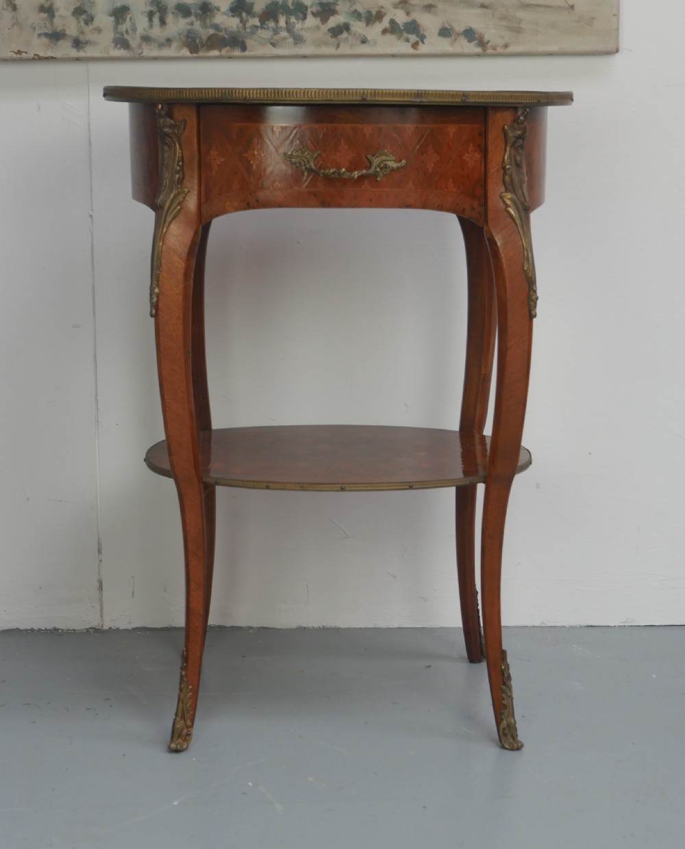 An oval Louis XV style wooden centre table featuring geometric parquetry inlay, a single drawer, a lower tier, cabriole legs, and ornate gilt metal mounts. View XV