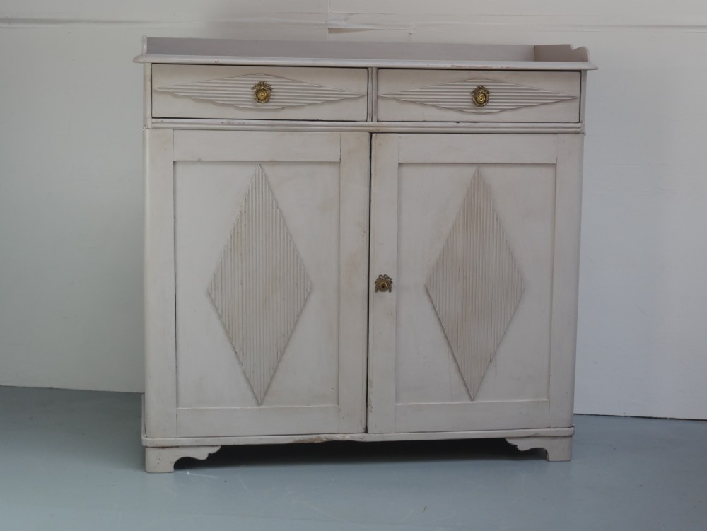 A pale grey painted Scandinavian cupboard featuring two carved drawers above two diamond-panelled doors with brass hardware. View II