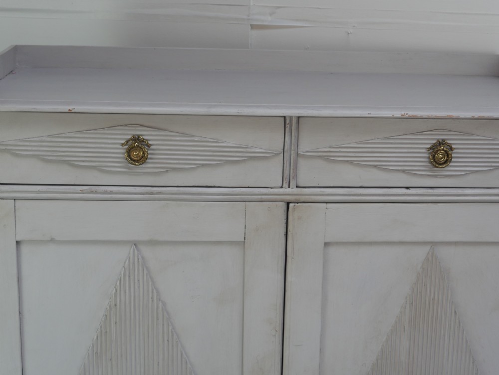 A pale grey painted Scandinavian cupboard featuring two carved drawers above two diamond-panelled doors with brass hardware. View III