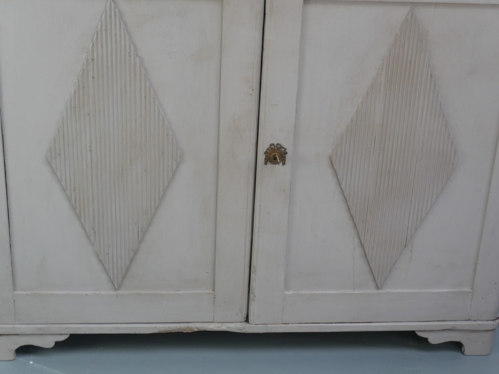 A pale grey painted Scandinavian cupboard featuring two carved drawers above two diamond-panelled doors with brass hardware. View IV