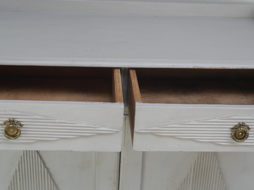 A pale grey painted Scandinavian cupboard featuring two carved drawers above two diamond-panelled doors with brass hardware. View VI