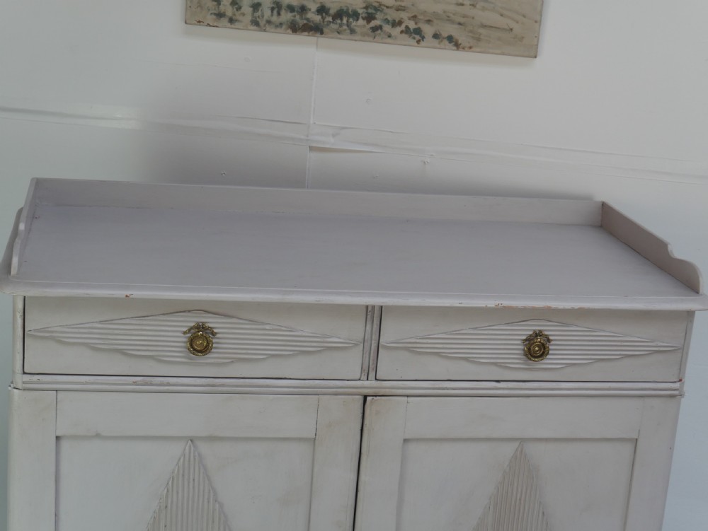 A pale grey painted Scandinavian cupboard featuring two carved drawers above two diamond-panelled doors with brass hardware. View VII