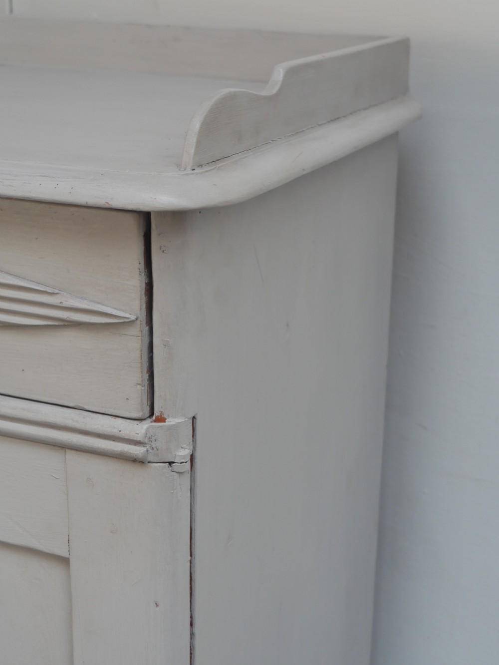 A pale grey painted Scandinavian cupboard featuring two carved drawers above two diamond-panelled doors with brass hardware. View XII
