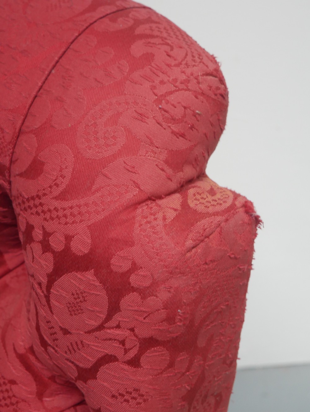 An antique Victorian Howard style armchair upholstered in red patterned damask fabric featuring a button-tufted backrest, low seat, and turned front wooden legs on brass castors. View III
