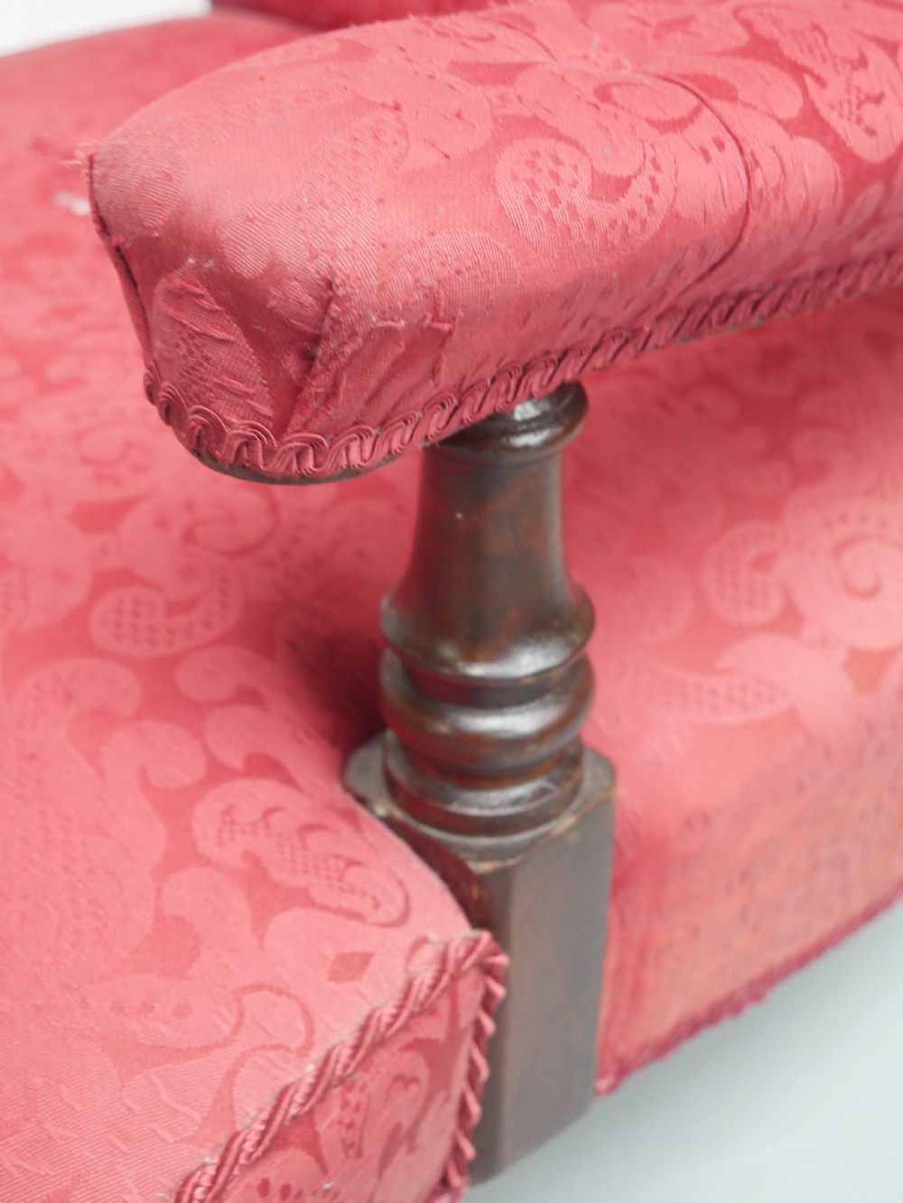 An antique Victorian Howard style armchair upholstered in red patterned damask fabric featuring a button-tufted backrest, low seat, and turned front wooden legs on brass castors. View X