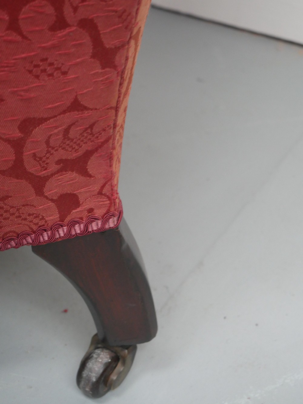 An antique Victorian Howard style armchair upholstered in red patterned damask fabric featuring a button-tufted backrest, low seat, and turned front wooden legs on brass castors. View XI