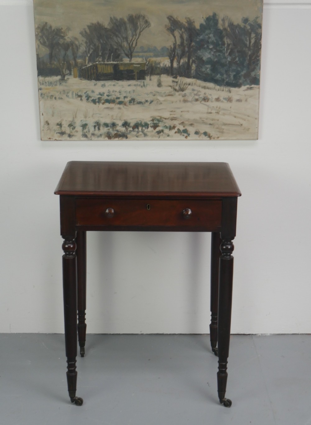 A dark mahogany Regency side table featuring a single drawer with turned knobs, a central brass keyhole, and turned legs terminating in castors.