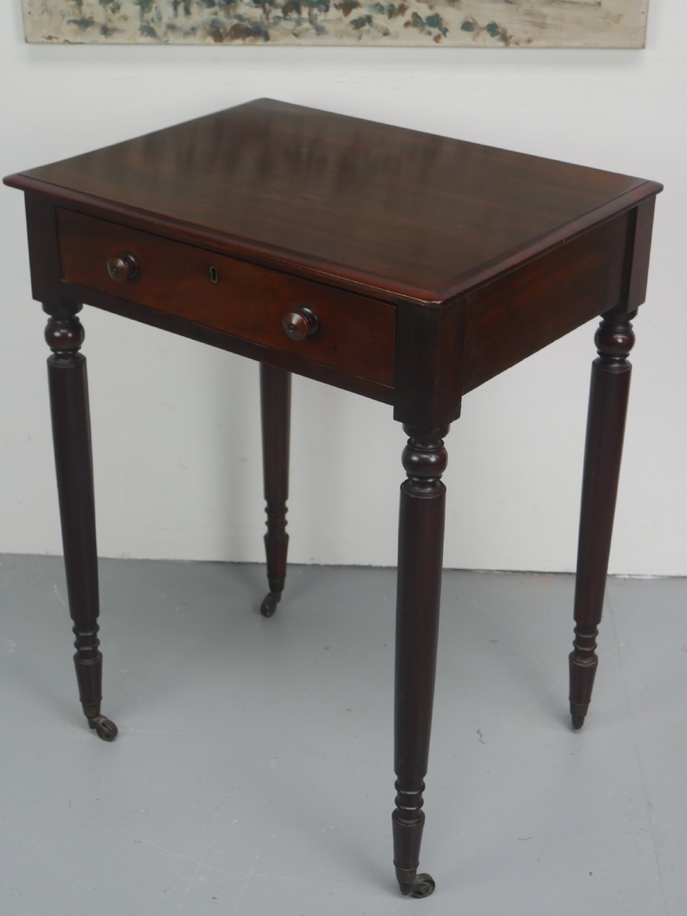 A dark mahogany Regency side table featuring a single drawer with turned knobs, a central brass keyhole, and turned legs terminating in castors. View IV