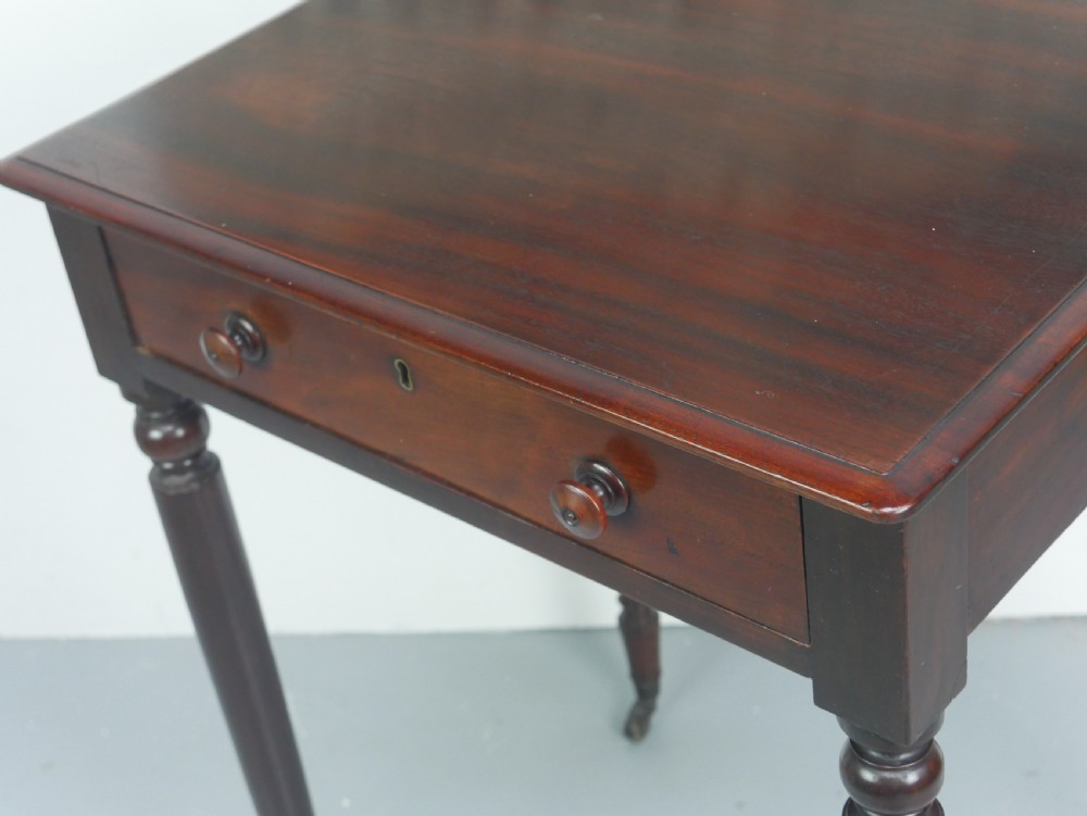 A dark mahogany Regency side table featuring a single drawer with turned knobs, a central brass keyhole, and turned legs terminating in castors. View V