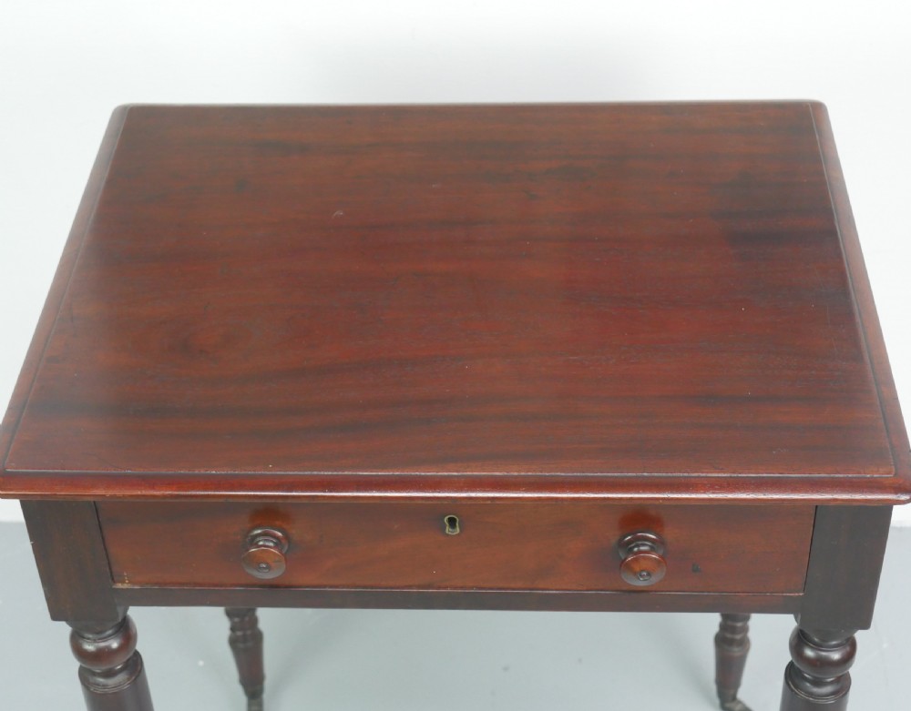 A dark mahogany Regency side table featuring a single drawer with turned knobs, a central brass keyhole, and turned legs terminating in castors. View VI