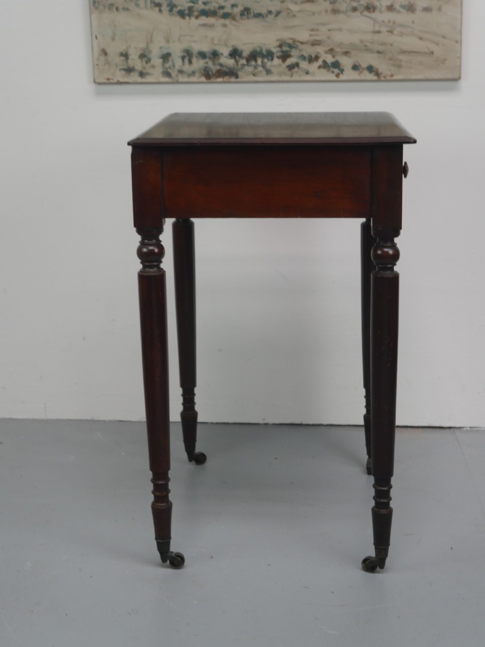 A dark mahogany Regency side table featuring a single drawer with turned knobs, a central brass keyhole, and turned legs terminating in castors. View VII