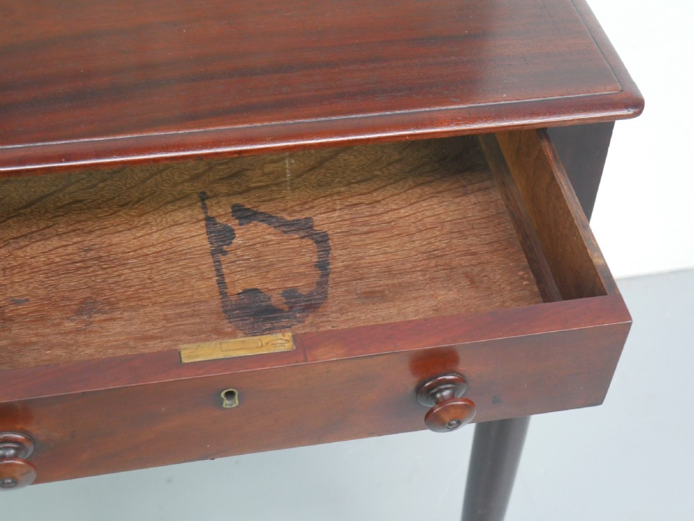 A dark mahogany Regency side table featuring a single drawer with turned knobs, a central brass keyhole, and turned legs terminating in castors. View X