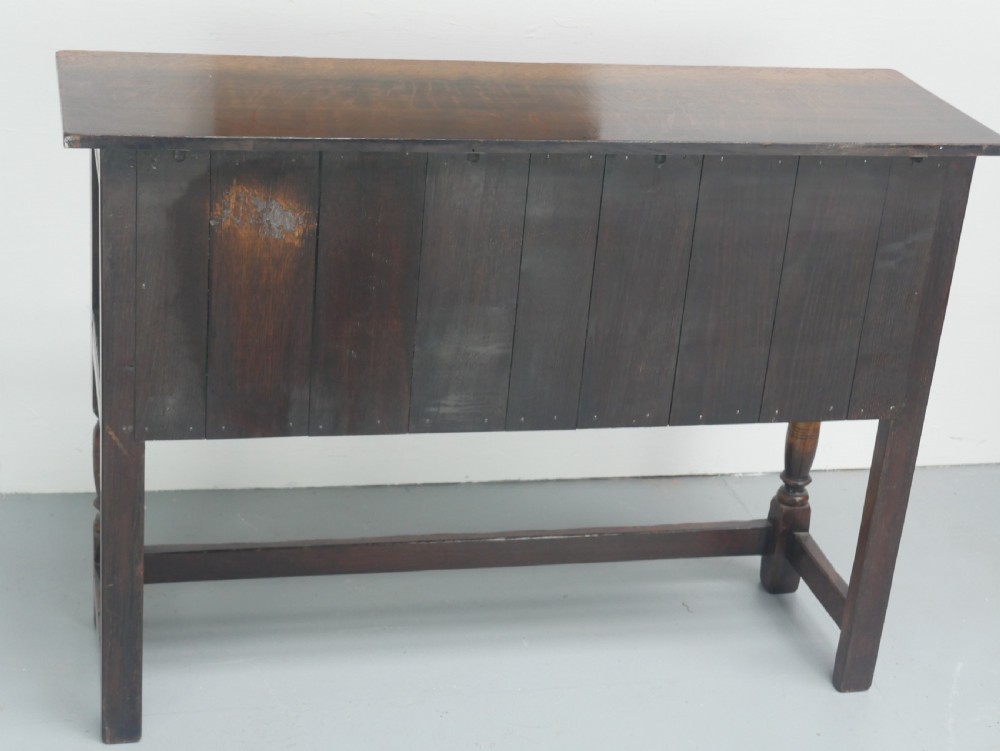 A small dark oak carved sideboard featuring panelled cupboard doors with carved arch motifs, iron hinges, and turned legs with a stretcher base. View IX