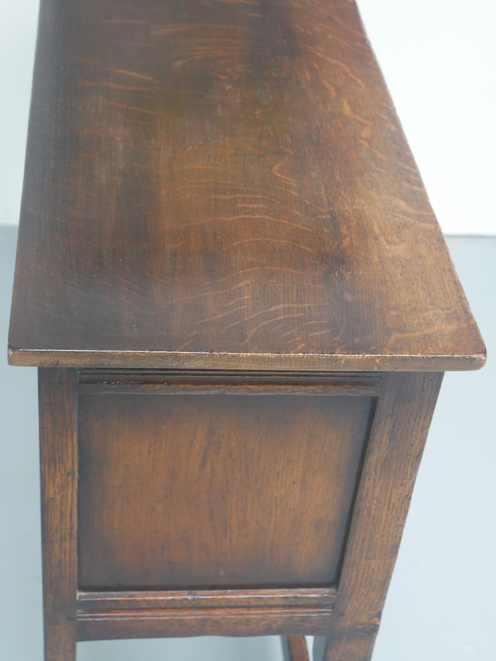 A small dark oak carved sideboard featuring panelled cupboard doors with carved arch motifs, iron hinges, and turned legs with a stretcher base. View XI
