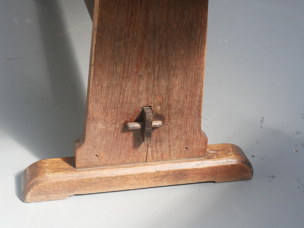 A long solid oak refectory dining table featuring a plank top, shaped trestle end supports, and a central pegged stretcher. View II