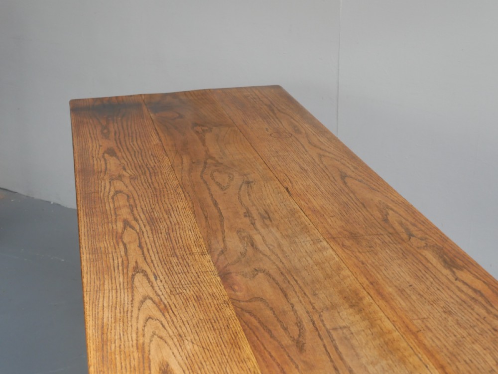 A long solid oak refectory dining table featuring a plank top, shaped trestle end supports, and a central pegged stretcher. View IV