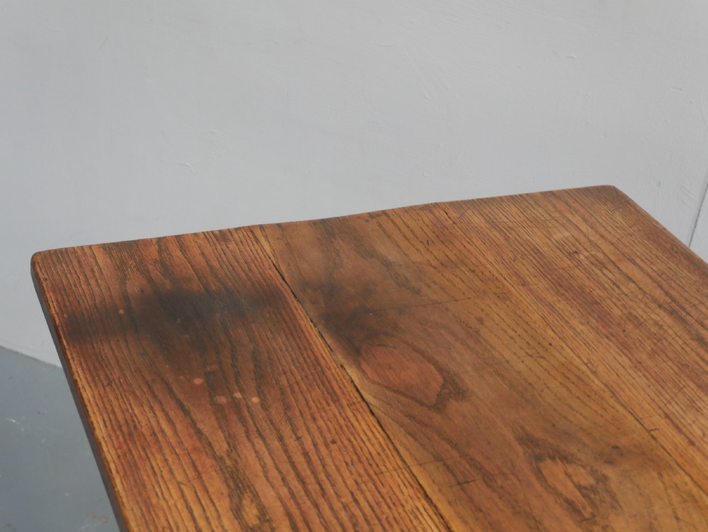A long solid oak refectory dining table featuring a plank top, shaped trestle end supports, and a central pegged stretcher. View V