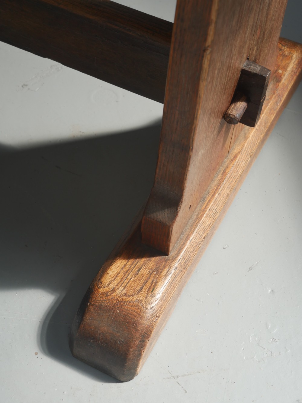 A long solid oak refectory dining table featuring a plank top, shaped trestle end supports, and a central pegged stretcher. View VII