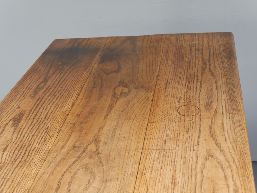 A long solid oak refectory dining table featuring a plank top, shaped trestle end supports, and a central pegged stretcher. View VI