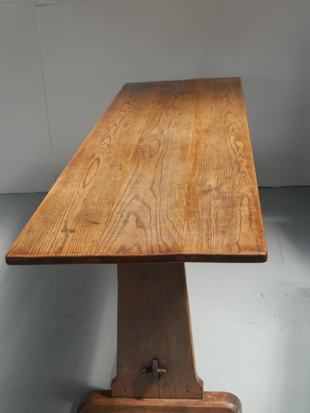 A long solid oak refectory dining table featuring a plank top, shaped trestle end supports, and a central pegged stretcher. View XI