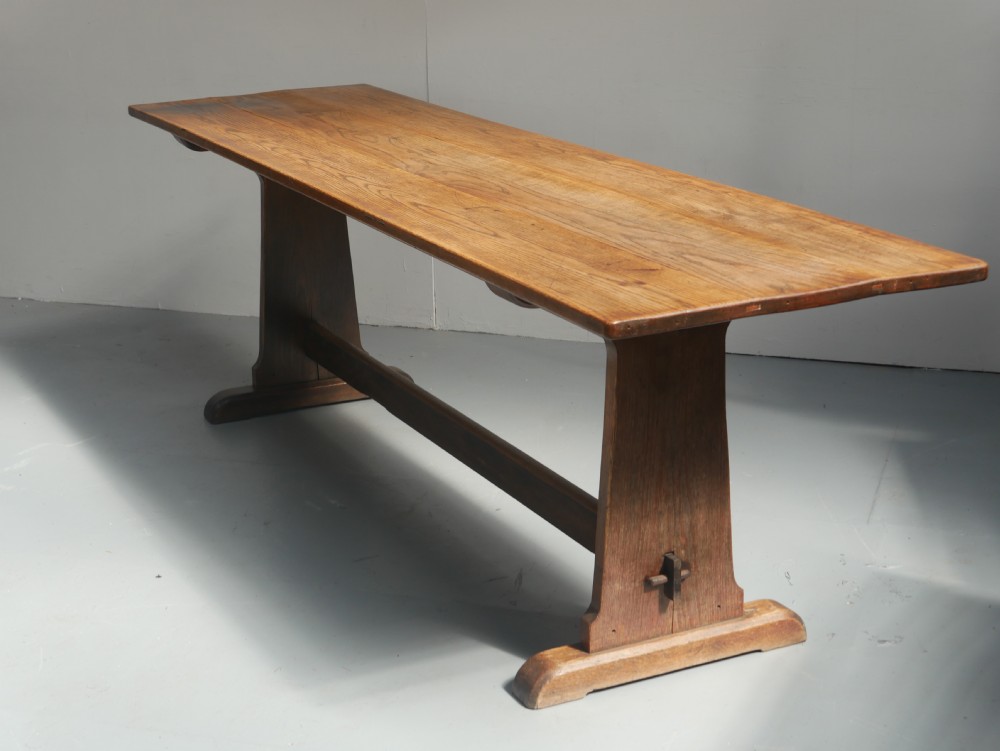 A long solid oak refectory dining table featuring a plank top, shaped trestle end supports, and a central pegged stretcher. View XIII