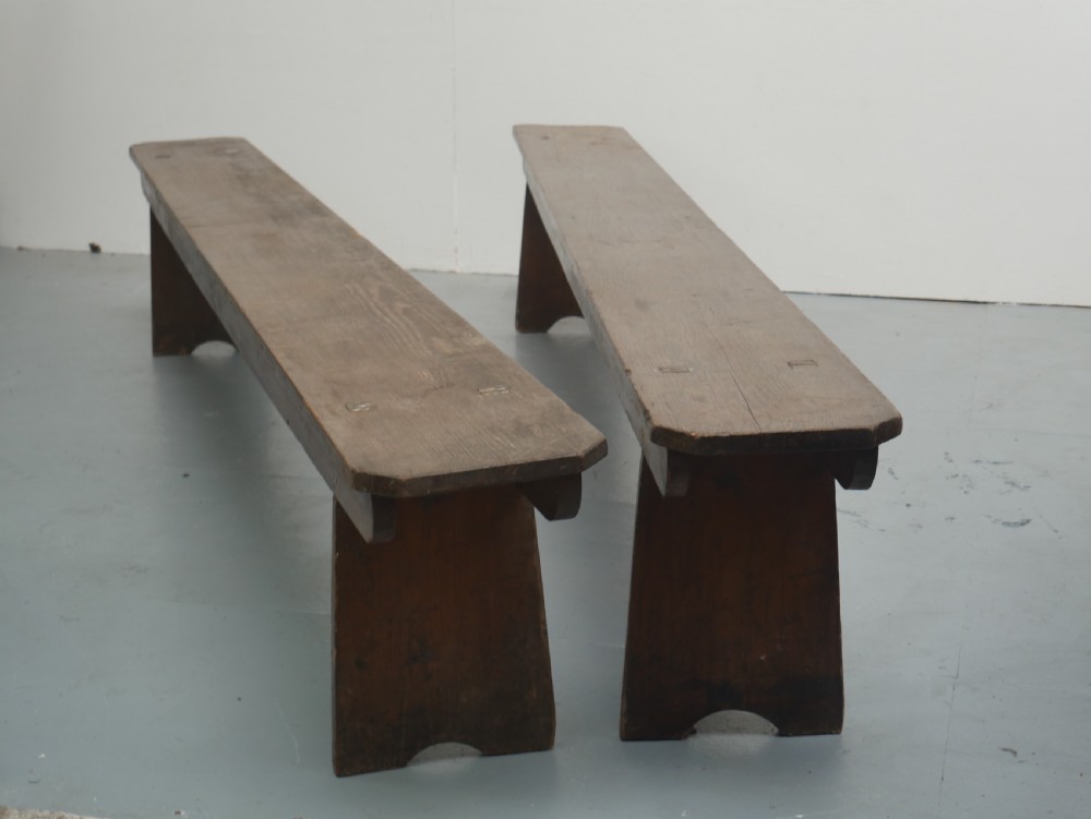 A pair of long, dark brown rustic pine benches featuring solid plank tops and trestle-style slab legs with arched cutouts.