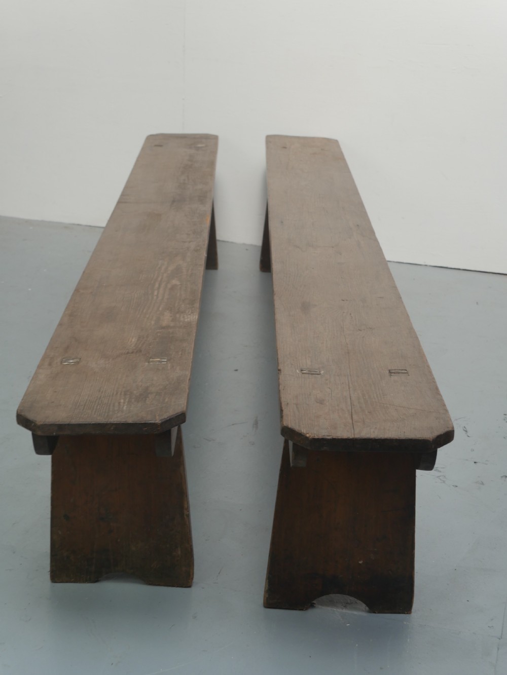 A pair of long, dark brown rustic pine benches featuring solid plank tops and trestle-style slab legs with arched cutouts. View VIII