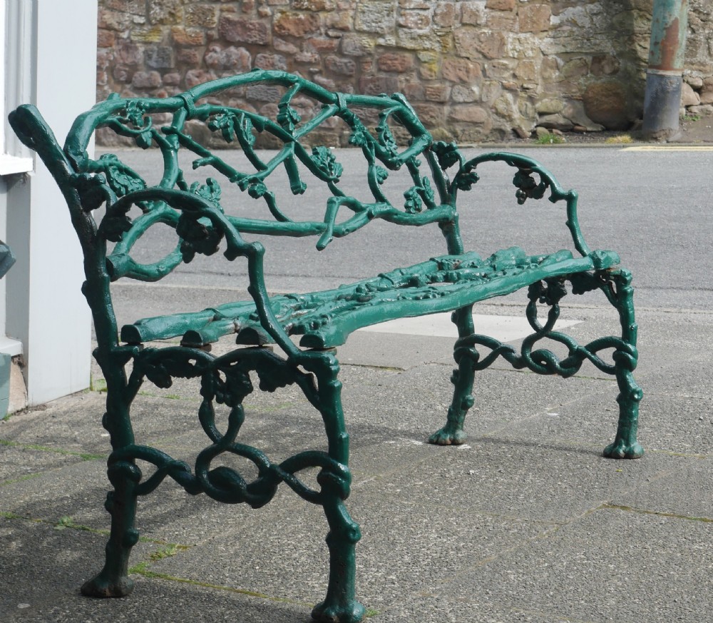 A green painted Victorian cast iron garden bench featuring a naturalistic organic branch and twig pattern.