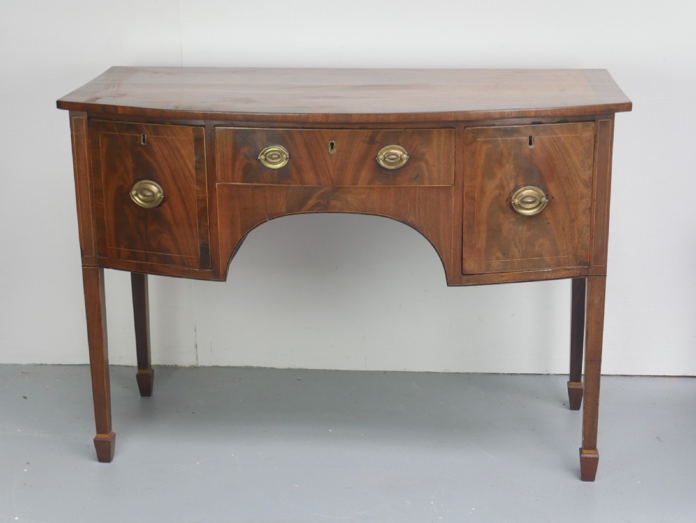 A small Georgian bowfront mahogany sideboard featuring an arched central apron, two side drawers with oval brass handles, and square tapered legs.