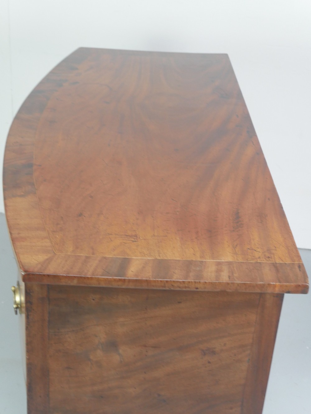 A small Georgian bowfront mahogany sideboard featuring an arched central apron, two side drawers with oval brass handles, and square tapered legs. View II