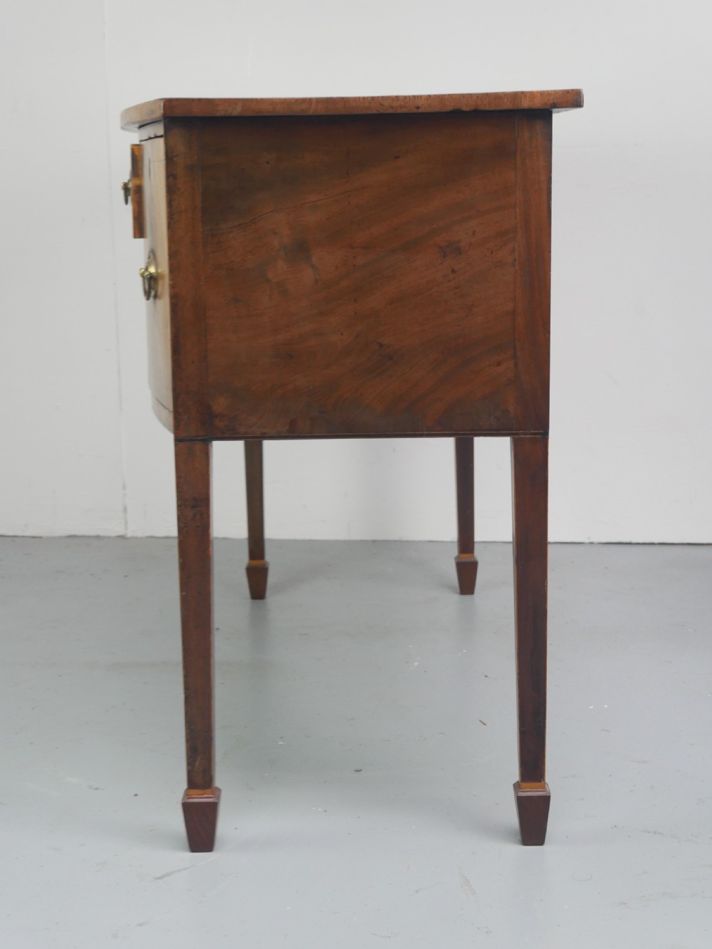 A small Georgian bowfront mahogany sideboard featuring an arched central apron, two side drawers with oval brass handles, and square tapered legs. View III