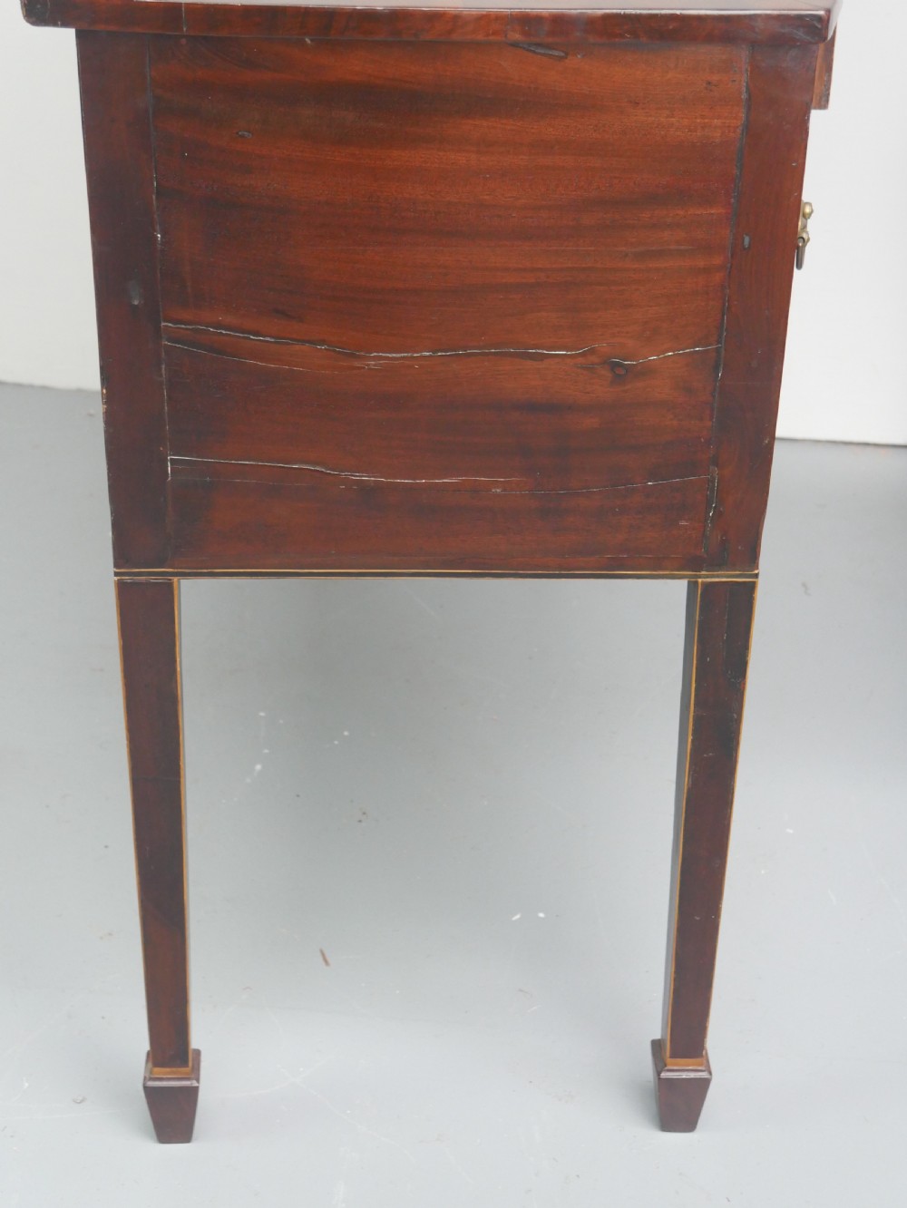 A small Georgian bowfront mahogany sideboard featuring an arched central apron, two side drawers with oval brass handles, and square tapered legs. View V