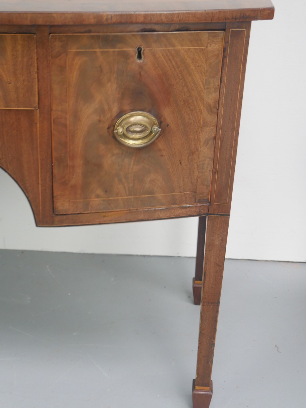 A small Georgian bowfront mahogany sideboard featuring an arched central apron, two side drawers with oval brass handles, and square tapered legs. View VII
