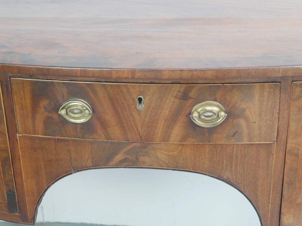 A small Georgian bowfront mahogany sideboard featuring an arched central apron, two side drawers with oval brass handles, and square tapered legs. View VIII