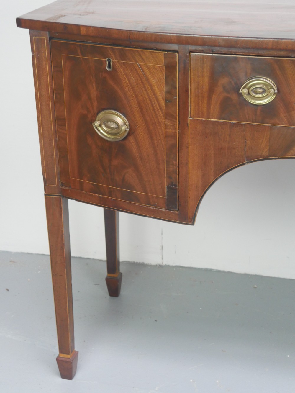A small Georgian bowfront mahogany sideboard featuring an arched central apron, two side drawers with oval brass handles, and square tapered legs. View IX