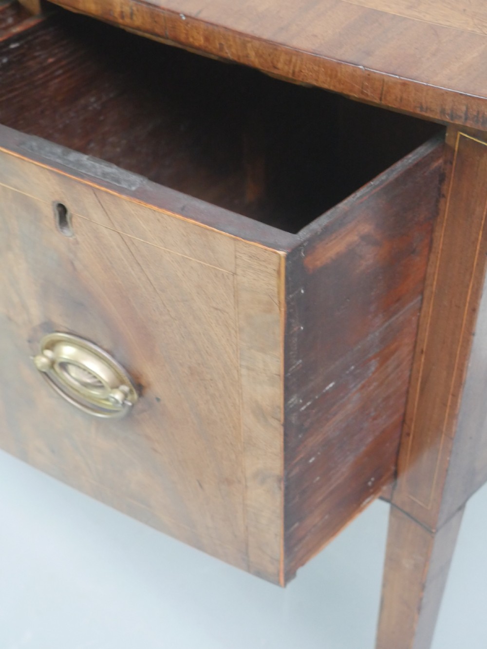 A small Georgian bowfront mahogany sideboard featuring an arched central apron, two side drawers with oval brass handles, and square tapered legs. View XII