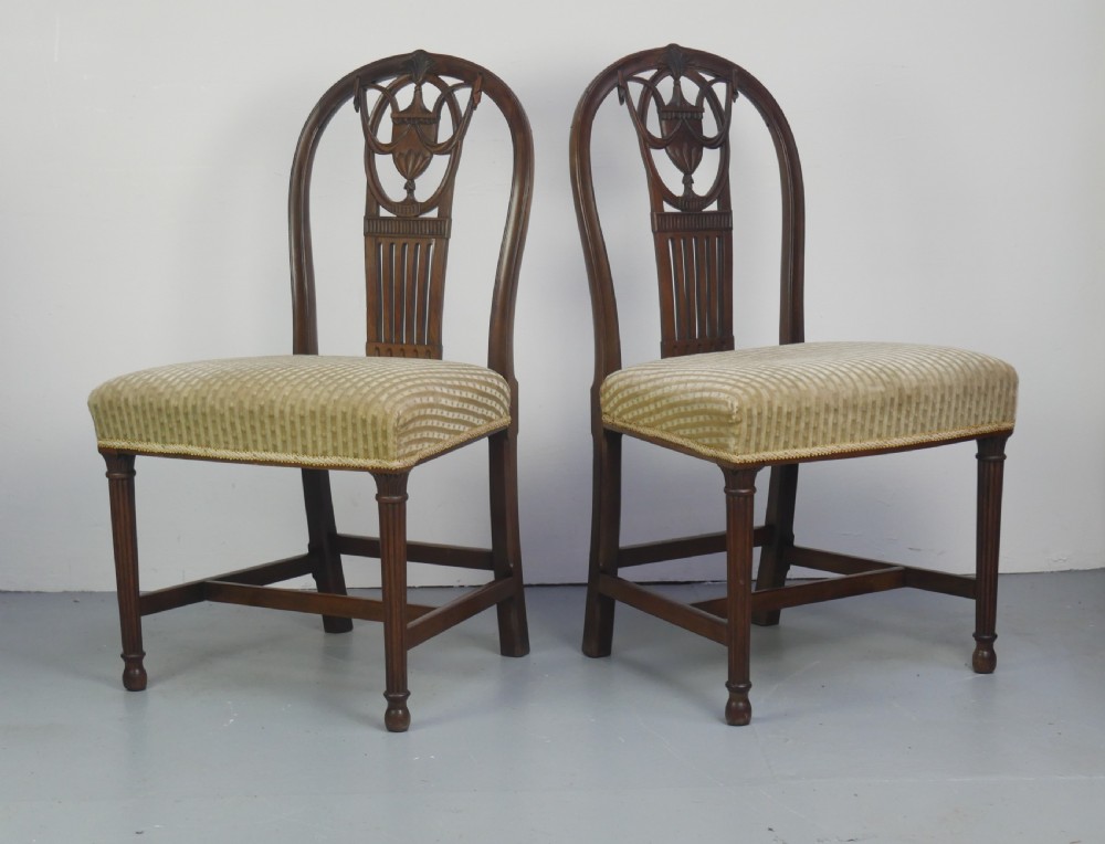 A pair of antique Georgian mahogany side chairs featuring pierced urn carved splats, arched backs, and upholstered seats supported by fluted front legs.