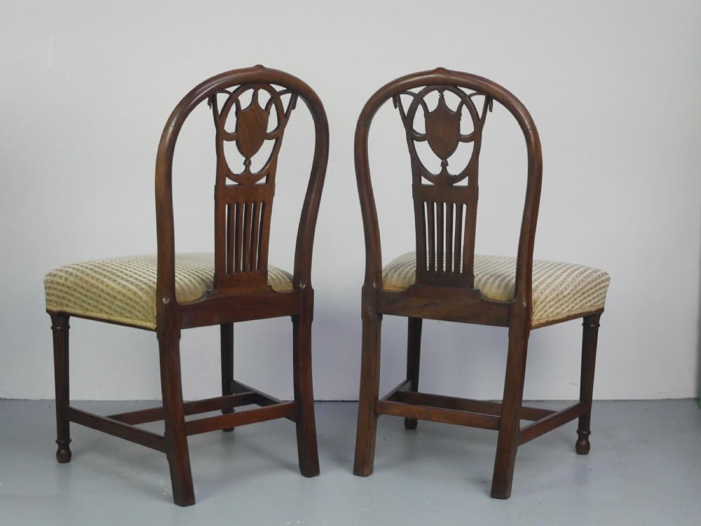 A pair of antique Georgian mahogany side chairs featuring pierced urn carved splats, arched backs, and upholstered seats supported by fluted front legs. View VII