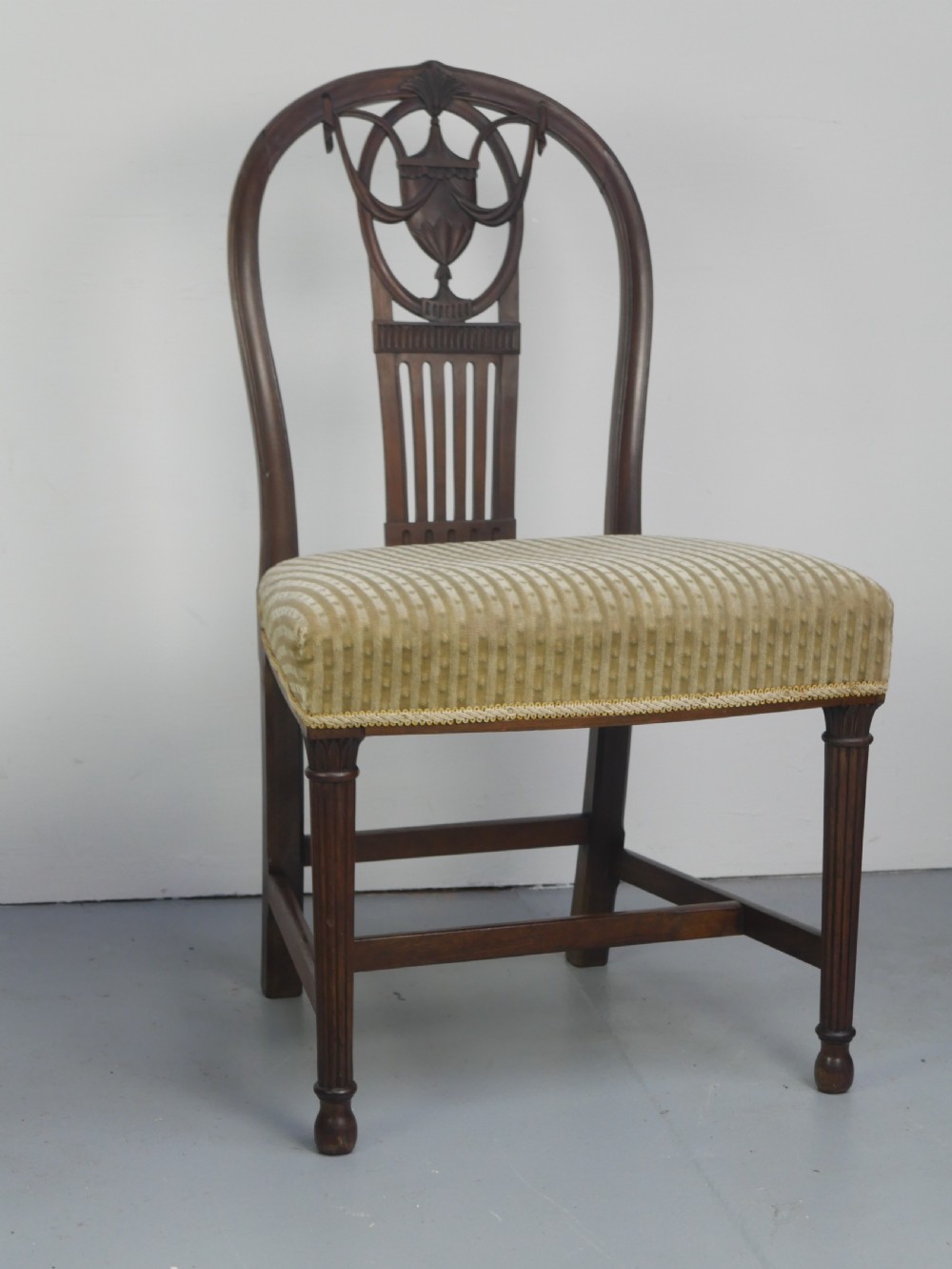 A pair of antique Georgian mahogany side chairs featuring pierced urn carved splats, arched backs, and upholstered seats supported by fluted front legs. View XXVI