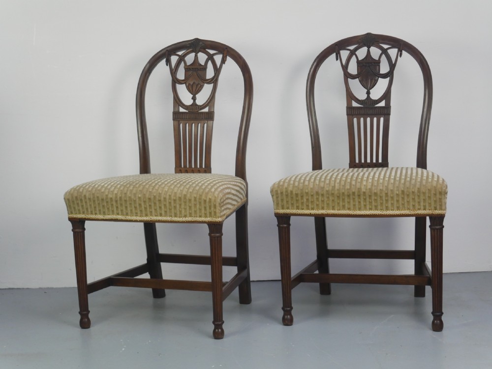 A pair of antique Georgian mahogany side chairs featuring pierced urn carved splats, arched backs, and upholstered seats supported by fluted front legs. View XXVII